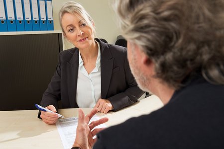 VdK-Beratung Eine Frau reicht einem Mann eine VdK-Beitrittserklärung. Sie sitzen sich in einem Büro gegenüber, im Hintergrund stehen viele Aktenordner im Regal.
