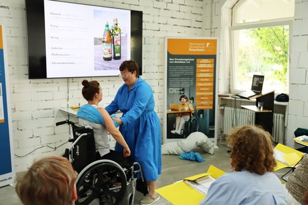 Seminarleiterin Tina Würzburger (rechts) zeigt den Teilnehmenden am Beispiel von Mitarbeiterin Susanne Sickert (links) rückenschonende Handgriffe.