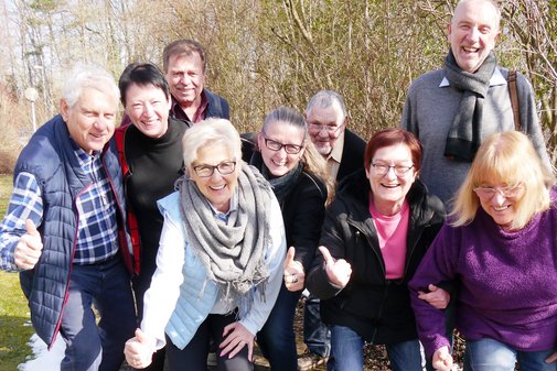 Neun VdK-Ehrenamtliche stehen auf einer Wiese. Im Hintergrund sind kahle Bäume. Sie lachen in die Kamera und geben einen Daumen nach oben.
