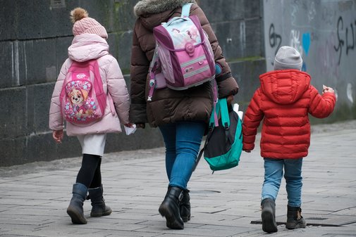 Eine Mutter (Mitte) geht mit ihren Kindern die Straße entlang.